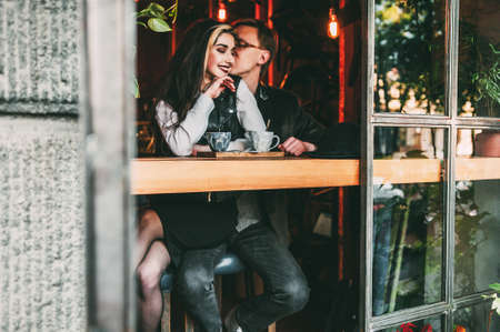 Young woman and man talking during first date in cozy coffee shop enjoying free time together,hipster girl checking notification on mobile while spending time with boyfriend having lovely conversationの写真素材