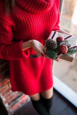 Female hands holding Christmas gift box on white wooden background with Fir branches, pine cones. Xmas and Happy New Year theme, bokeh, sparking, glowing.の写真素材