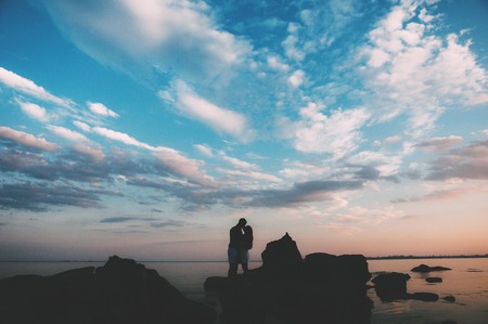Romantic couple silhouettes on the beach, caressing each other with the sea and a beautiful colorful sunset in the background.の写真素材