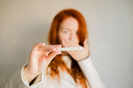 Girl in a mask from a virus with a thermometer in her hands. Coronovirus epidemic. Temperature, thermometer.の写真素材