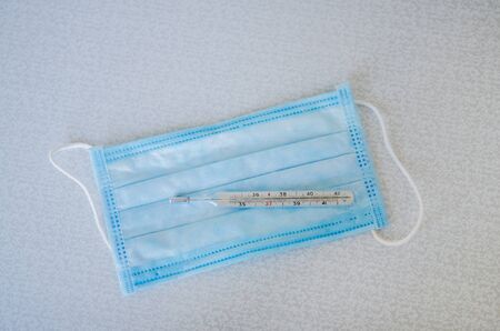 Surgical mask and thermometer on a light background.