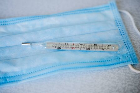 Surgical mask and thermometer on a light background.