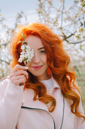 Redhead girl. Portrait on a background of a blooming garden and spring trees.