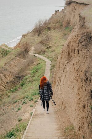 Beautiful red-haired girl goes down the stairs to the sea in springの写真素材