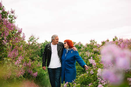 A loving married couple walks in a lilac grove at sunset in the spring. Retired couple. A woman with...