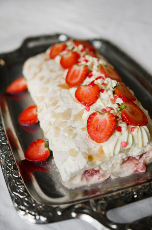 Meringue roll with almond flakes on a beautiful background. Summer Pavlova dessert with delicate cream, decorated with strawberries and creamの写真素材