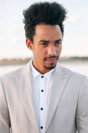 A handsome dark-skinned African American man in a light suit with his bright red cabliolet car. The...