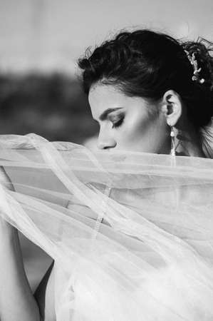 Black and white portrait of a beautiful girl in a dress with a veil close-up. The wind develops hair...