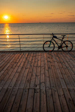 Bicycle against the background of a contrasting, bright, juicy sunrise or sunset by the sea, in orange tones.の写真素材