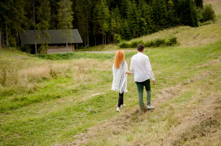 Portrait of a happy young woman holding her boyfriend's hand while walking in the mountains on vacation. Couple enjoying a hike in nature.の写真素材