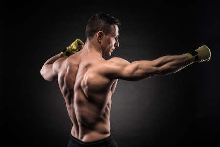 Muscular young man in boxing gloves and shorts shows the different movements and strikes in the studio on a dark backgroundの写真素材
