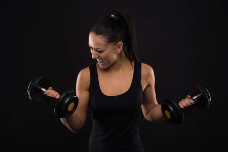 Young sportslooking nice lady with dark hair shows various performs exercises with equipment on the black background in studioの写真素材