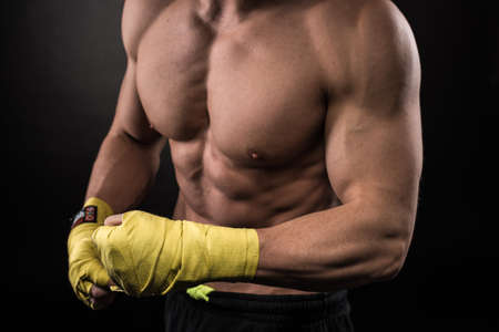 Muscular young man in boxing gloves and shorts shows the different movements and strikes in the studio on a dark backgroundの写真素材