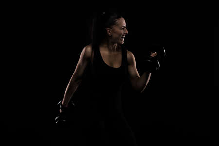 Young sportslooking nice lady with dark hair shows various performs exercises with equipment on the black background in studioの写真素材