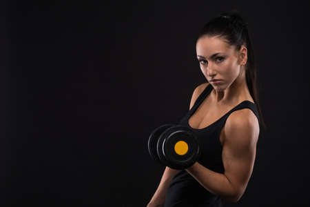 Young sportslooking nice lady with dark hair shows various performs exercises with equipment on the black background in studioの写真素材