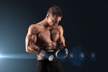 Muscular young man in boxing gloves and shorts shows the different movements and strikes in the studio on a dark backgroundの写真素材