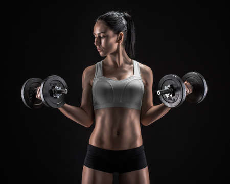 Fitness girl with dumbbells on a dark backgroundの写真素材