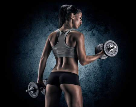 Muscular young woman in studio on dark background shows the different movements and body partsの写真素材