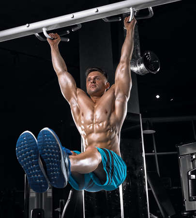 Young handsome guy with a naked torso doing exercises in the gym