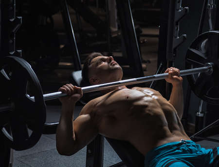 Young handsome guy with a naked torso doing exercises in the gym