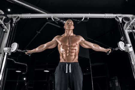 Young handsome guy with a naked torso doing exercises in the gym