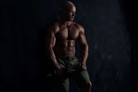 Muscular bodybuilder guy doing exercises with dumbbell over black backgroundの写真素材