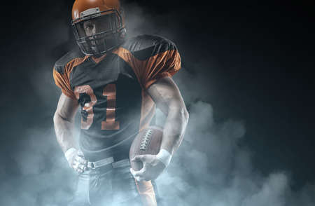 American football player on a dark background in smoke in black and orange equipment.の写真素材