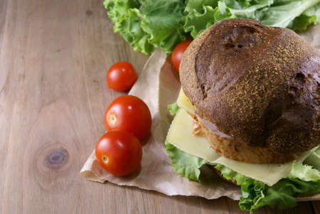 Picnic, burger with meat, cheese and fresh vegetables is lying on a rustic wooden table.