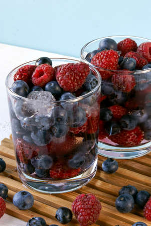 Cooled by ice juicy summer berries in glasses: raspberries, blueberries, bilberries. Rustic white table.の写真素材