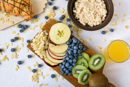 Oatmeal with kiwi, apples, almonds and blueberries. Amended orange juice in a glass, croissant and fresh fruits. A healthy breakfast on a light table, top viewの写真素材