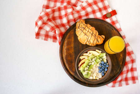Light and healthy breakfast: oatmeal with fruit and berries, orange juice, croissant. On the white table, top viewの写真素材