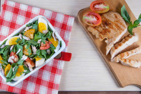 Chicken fillet, grilled, with a large portion of salad with fresh vegetables and herbs on a wooden...
