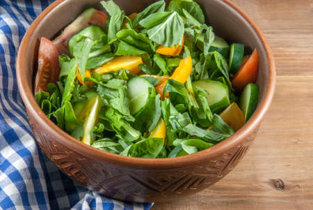 A large portion of salad with fresh basil leaves, arugula, parsley, tomatoes. On a wooden table with a tablecloth.の写真素材