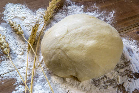 The finished raw dough on a wooden table, spikelets of wheat