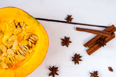 Half of pumpkin and spices for its cooking on a white wooden backgroundの写真素材