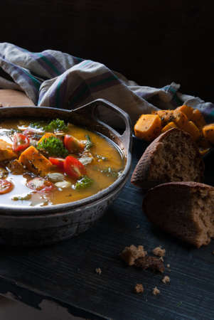 Pumpkin soup with tomatoes and herbs in a rustic style. Near fragrant broken down into bits and pieces of black breadの写真素材