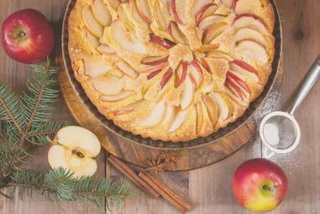 Traditional apple pie on a wooden table, with apple and powdered sugar. Near the Christmas tree...