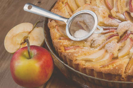 Traditional apple pie on a wooden table, with apple, powdered sugar, tonedの写真素材