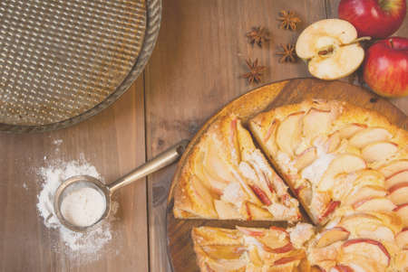 Traditional apple pie on a wooden table, with apple, powdered sugar and spices, tonedの写真素材