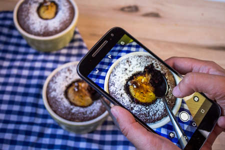 Girl shoots food with a smartphone. Hands with a smartphone. On the table is chocolate dessert with pearsの写真素材
