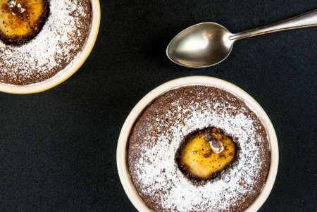 Two chocolate desserts with a pear on a black stone table, top view