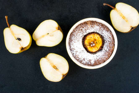 Chocolate dessert with a pear on a black stone table, sliced ??pear close, top view
