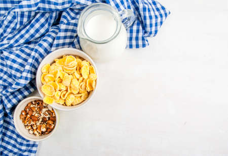 Light healthy breakfast: cornflakes, milk and nuts for them. On wooden white table, top view, copy spaceの写真素材