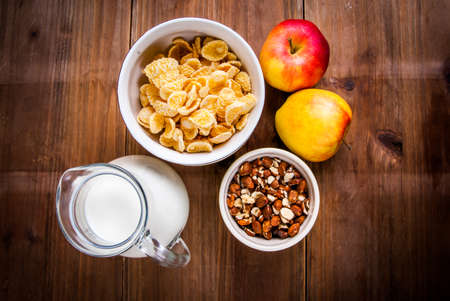 Light healthy breakfast: cornflakes, milk, apples and nuts for them. On wooden rustic table, top view, copy spaceの写真素材