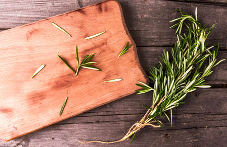 Sprig of rosemary on a wooden table next to a cutting board, top viewの写真素材