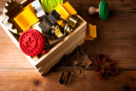 Cookie cutters for making Christmas cookies and stamps in a wooden box and scattered on the wooden table. One stamp with "Happy Holiday" sign (in German)の写真素材