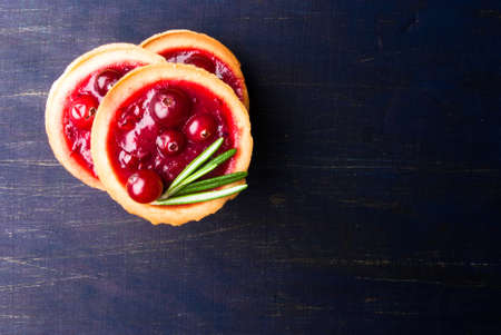 Winter one bite-sized snack or dessert: tartlets with sweet and sour cranberry sauce (jam), decorated with rosemary. Top view, copy spaceの写真素材