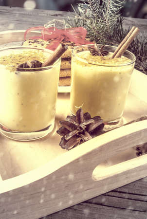 Traditional Christmas drink eggnog and cookies on a wooden background surrounded by Christmas tree...