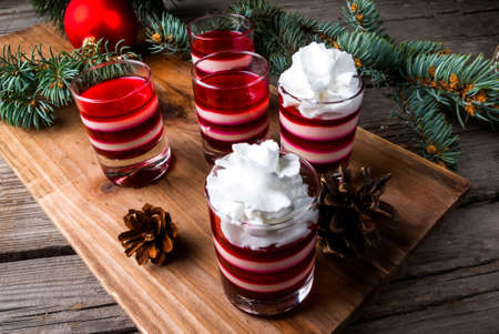Christmas dessert, striped jelly in the style of Christmas candy, white and red, with whipped cream. Against the background of Christmas tree branches and Christmas decorationsの写真素材