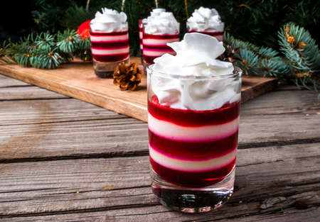 Christmas dessert, striped jelly in the style of Christmas candy, white and red, with whipped cream. Against the background of Christmas tree branches and Christmas decorationsの写真素材